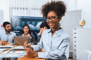 Arka plandaki ekranda bir grup ofis çalışanı ile görüşürken gözlük takan mutlu Afrikalı genç iş kadını. Takım toplantısında kendine güveni tam bir ofis hanımı. Uyum