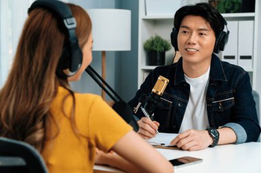 Gülümseyen radyo etkili sunucusu kulaklık takıyor kadın konuşmacı ile röportaj yapıyor sosyal medya internet sitesinden dinleyicilere bilgi paylaşıyor stüdyo kaydında sabah canlı yayın kanalı. İnfobahn.