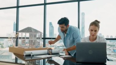 Akıllı mimar mühendis ev modelini incelerken meslektaşı da laptop analiz verilerini kullanıyor. Modern ofisteki ev modeli inşaatında profesyonel tasarımcı takımı birlikte çalışıyor. İzleme