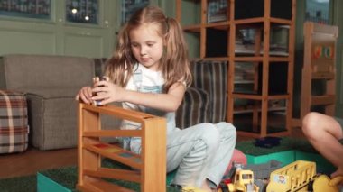 Kafkas kız kum havuzunda otururken araba modelini bayır oyuncağına yerleştiriyor. Çeşitli çocuklar oyun odasında teneffüste okulda otururken plastik modelcilik oynuyorlar. Yaratıcı aktivite konsepti. Etkinlik.