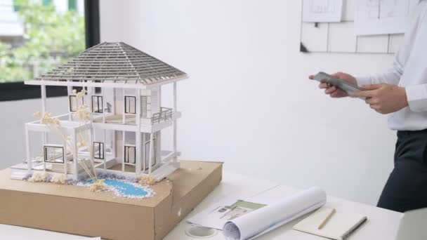 专业英俊的亚洲项目经理使用平板电脑检查房屋模型 同时在办公室仔细检查房屋模型结构 并将图纸从后面剥去 创意设计 纯洁无瑕 — 图库视频影像