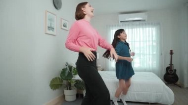 Yatak odasında Asyalı kızıyla müzik eşliğinde dans eden mutlu çekici anne. Beyaz anne dans eder ya da egzersiz yapar. Bu arada tatlı çocuk da müzik eşliğinde yatağa atlar. Aile eğlence konsepti. Pedagoji.