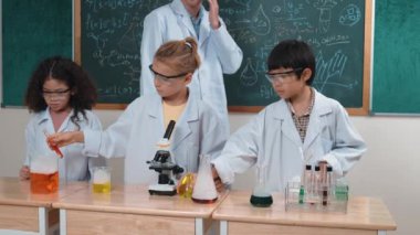Amerikalı bir kız renkli sıvıyı incelerken erkek beher içine solüsyon döker. Enerjik öğrenci, öğretmenler çocukları keşfederken ve yenilikleri keşfederken arkadaşının deney yapmasına destek oluyor. Pedagoji.
