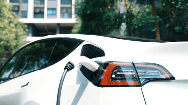 Yazın yeşil sürdürülebilir şehir bahçesinde elektrikli araba şarj oluyor. Kentsel sürdürülebilirlik yaşam tarzı yeşil temiz yeniden şarj edilebilir enerji elektrikli BEV araç iç organları