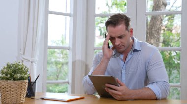 İş adamı, evde dizüstü bilgisayarla iş problemini çözmeye çalışıyor, evde masasında oturmuş, stresli ve hayal kırıklığına uğramış bir ifadeyle probleme çözüm bulmaya çalışıyor. Eşzamanlama