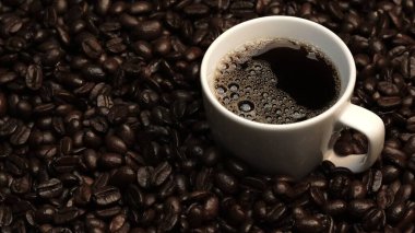 Kahve ya da kahve çekirdekli espresso manzarası. Taze kavrulmuş kahve çekirdeğini yakın çekimde ahşap masanın etrafına bir fincan americano ve aromatik akarsu ve tohum dumanı serpin. Geliştirilebilir.