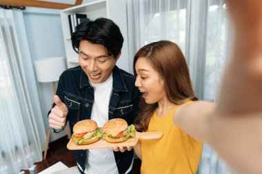 Gülümseyen sunucu şefler akıllı telefonlarıyla fotoğraf çekiyorlar. Özçekim yoluyla. Yemek programında çift hamburger tutuyorlar. İnfobahn.