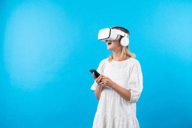Kafkasyalı bir kız elinde telefon tutarken ve görüş açısını gösterirken VR gözlük takıyor. Görsel gerçeklik dünyasını ya da metaevreni keşfetmek isteyen mutlu kadın şaşırdı. Teknoloji yeniliği. Kısıtlanma.