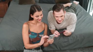 Genç çift, kredi kartıyla ödemek için internet üzerinden ödeme uygulaması ve dijital cüzdan kullanarak yatak odasında oturuyor. Mobil internet üzerinden alışveriş ve modern alımlar. Düzenle