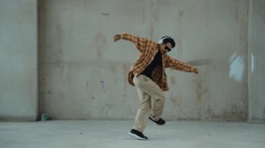 Çimento arka planında kulaklıktan müzik dinlerken sıradan sokak dansı yapan çekici İspanyol dansçı. Break dans gösterisinin hareketli çekimi. Açık hava sporu 2024 hiphop..