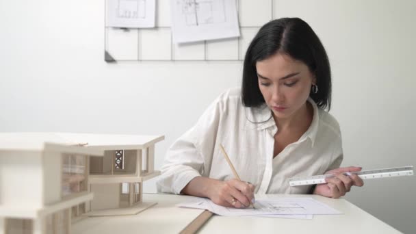 美しい若い建築家エンジニアのクローズアップは 鉛筆のマーキングポイントとルーラーを使用して ブループリントで現代のオフィスで家のモデルを測定することに焦点を当てています クリエイティブデザインと建築コンセプト インマキュライト — ストック動画