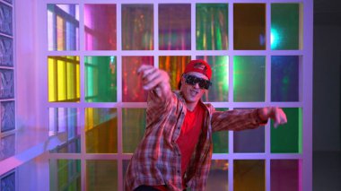Komik break dansçı kameraya bakarken hiphop 'a doğru serbest adım atıyor. Çılgın mutlu hipster dans edip sokak dansı yaparken Led ışığında günlük kıyafet ve güneş gözlüğü takıyor. Mutluluk.