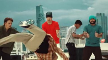 Profesyonel Asyalı sokak dansçısı çatıda çok kültürlü arkadaşlar dans ederken B boy dansı yapıyor. Genç modern dans grubu hip hop hareketi yapıyor. Tarz, moda, aksiyon. Açık hava sporu 2024 hiphop..