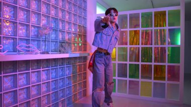 Gece kulübünde kameraya bakarken güneş gözlüklü Asyalı dansçı serbest dans ediyor. Mutlu sokak dansçısı dans ediyor ve renkli parlak neon ışığı ya da yol gösteren ışıkla ayak seslerini gösteriyor. Mutluluk.