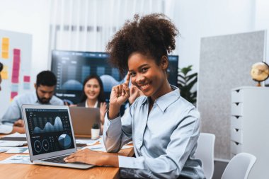 Bir grup ofis çalışanı ile birlikte arka planda ekranda gösterim paneliyle buluşan mutlu Afrikalı genç bir iş kadını portresi. Takım toplantısında kendine güveni tam bir ofis hanımı. Uyum