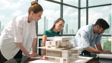 Beyaz proje yöneticisi dizüstü bilgisayar analiz verilerini kullanırken, mimar mühendis ekibi ev modeli inşaatını analiz etmek için birlikte çalışıyor. Bir grup tasarımcı ev tasarımı hakkında konuşuyor. İzleme