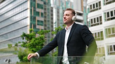 Kulaklıklı yönetici çatıda dururken müzik dinlemekten zevk alır. Rahatlamış yatırımcı kulaklık takıyor ve modern gökdelen manzarasına bakarken kafiyeli müzik çalıyor. Yaşam tarzı. Urbane.