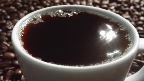 将新鲜的浓缩咖啡倒入白杯中 倒入一堆咖啡豆 在杯子里倒入黑咖啡 配上褐色背景 种子撒在木制桌子上 靠近点顶部视图 可赔偿性 — 图库视频影像