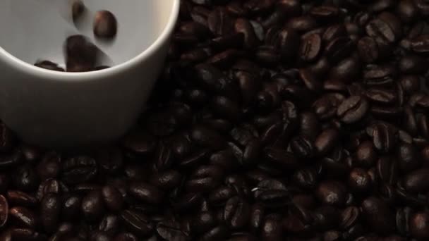 靠近咖啡豆掉到咖啡杯里 周围堆满了咖啡豆 把香喷喷的豆子倒入白杯中 顶部的咖啡下降到玻璃与黑色背景 可赔偿性 — 图库视频影像
