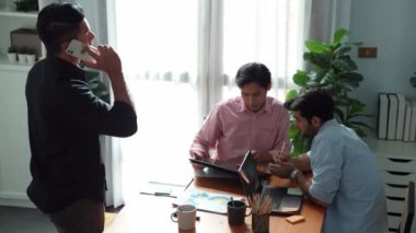 Proje yöneticisi toplantı odasında telefonla konuşurken beyin fırtınası fikriyle birlikte çalışan ekibin üst görüntüsü. Erkek lider yatırımcıyı arıyor ve ekip stratejisini tartışırken mevcut planı sunuyor. Cemaat.