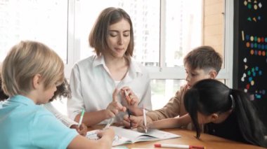 Çizim kitabında işaret kullanarak çeşitli öğrencilerin ve zeki öğretmen çizimleri ve boyamaları mutlu olsun. Çok kültürlü, zeki bir öğrenci yetenekli beyaz bir eğitmenle konuşurken çizim kitabı kullanıyor. Etkinlik.