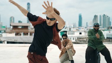 Bir grup profesyonel hip hop dansçısı çatıda break dans yapıyor. Becerikli koreograf serbest stil hareketini gösterirken, arkadaş da cesaretlendirir, alkışlar, alkışlar. Açık hava sporu 2024. ÇalışmaComment.