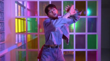 Kameraya bakarken kollarını esneten seksi kıyafetli Asyalı dansçı. Profesyonel sanatçı gece kulübünde renkli neon ışıkları canlı bir şekilde dururken serbest stil dansı yapıyor. Mutluluk.