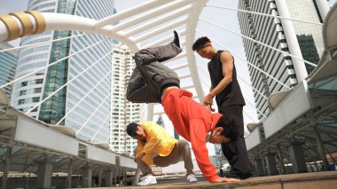 Asyalı hippi şehir merkezinde dans ederken profesyonel mutlu sokak dansçıları grubu neşelenin. Düşük açılı kameralı insanlarla çevrili. Break dans konsepti. Açık hava sporu 2024. Yumuşak bir şekilde..