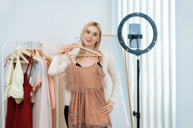 Genç sosyal medyum kadın moda videosu yapıyor. Blogcu kameraya ve ışık çemberine gülümserken, aynı zamanda ikna edici çevrimiçi kıyafetleri izleyicilere veya takipçilere vlog sattırıyor. Blithe