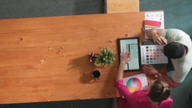 Renk paletinden renk seçmek için birlikte çalışan iş adamlarının üst düzey hava görüşü. İşadamı logo grafiğine bakarken pazarlama ekibine tablet kullanarak yönetici fikri sundu. Sempozyum.