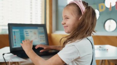Gülümseyen kız program sistemi ya da STEM teknoloji eğitiminde kodlama programı. Laptop yazma kodunu kullanarak çalışırken kulaklık takan bir çocuk kameraya bakmak için arkasını döner. Etkinlik.