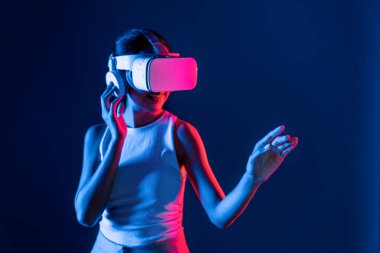 Çevresi siberpunk neon ışıklarıyla çevrili zeki bir kadın metaevrene bağlı VR kulaklık takıyor, gelecekçi siber uzay topluluğu teknolojisi. Sanal objeye el ile dokunan kadın. Halüsinasyon.