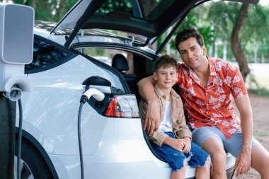 Elektrikli araçla aile gezisi, baba ve oğul EV 'yi yeşil ve temiz enerjiyle şarj ediyor. Sürdürülebilir çevre için doğa ve çevre dostu arabayla seyahat. Kalıcı