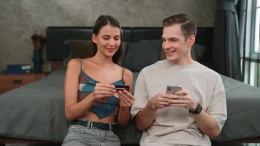 Genç çift, kredi kartıyla ödemek için internet üzerinden ödeme uygulaması ve dijital cüzdan kullanarak yatak odasında oturuyor. Mobil internet üzerinden alışveriş ve modern alımlar. Düzenle