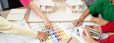 Yetenekli mimar takımı ev inşaatı hakkında tartışırken, iç mimar ev modeli ve bina planının dağıldığı renk paletine uygun bir renk belirliyor. Üst Manzara. Değiştirilmiş.