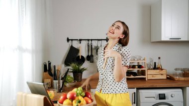 Kafkasyalı anne, modern mutfakta dizüstü bilgisayarda yemek tarifine bakarken salata yapmak için yemek hazırlıyor. Yetenekli ev bekçisi taze sebze kullanarak kahvaltı hazırlıyor. Pedagoji.