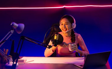 Geceleri podcast 'te olumlu konuşmalar yapan, pembe neon ışıklı modern stüdyoda sunum için dizüstü bilgisayar kullanan, gülümseyen, genç, güzel Asyalı bir etkileyiciydi. Taktik.