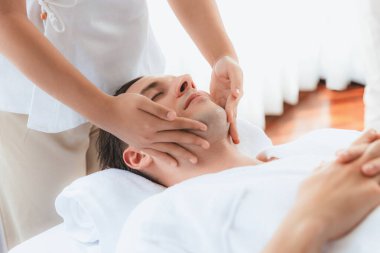 Beyaz adam stres önleyici kafa masajından ve lüks bir tatil beldesi veya otel spa salonundaki modern ışık ortamında yüz güzelliği eğlencelerini şımartmaktan hoşlanıyor. Sessiz.