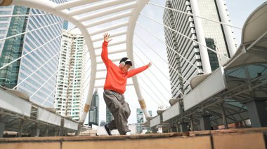 Şehre atlarken kulaklık takan Asyalı hippi. Profesyonel break dansçı şehirde break dans gösterisi yapıyor. Break dans ya da sokak dansı. Açık hava sporu 2024. Yumuşak bir şekilde..