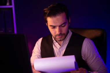 Stresli akıllı işadamı, gece geç saatlerde Mor Neon Koyu Işık Odası 'ndaki disiplin ürünleri servisinin çevrimiçi satış kanalını oluşturmak için kağıt işi raporu klasöründeki pazar verilerini analiz ediyor. Tahmin et..