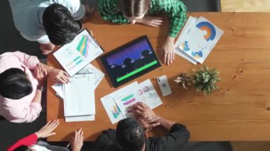 İş adamının tablet ekranını kullanmasına ilişkin en iyi bakış açısı artan grafiği kullanırken, farklı pazarlamacılar da fikir paylaşımı veya planlama stratejisini borsa istatistikleri etrafa saçılmış bir şekilde toplantı masasında paylaşıyorlar. Cemaat.