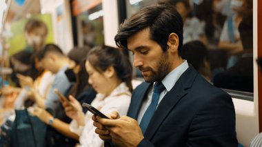 Gülümseyen beyaz iş adamı cep telefonuna bakıyor ya da trende otururken sosyal medya oynuyor. Çekici proje yöneticisi yoğun saatlerde toplu taşıma araçlarını kullanarak iş yerine gidiyor. Sevinçli..
