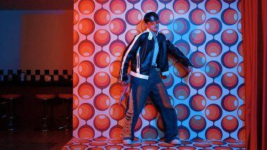 Asyalı break dansçı serbest stile geçiyor ve balon arka planlı kameraya bakıyor. Profesyonel hippi gündelik kıyafet giyer ve gözlük takar. Mutluluk.