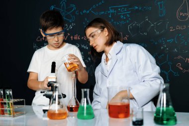 Öğretmen, laboratuarda öğrenciyi destekliyor. Öğrenci ve öğretmen cam kapta sıvı kullanarak STEM sınıfında kimya bilimi üzerine deney yapıyorlar. Karıştırma çözeltisi. Etkinlik.