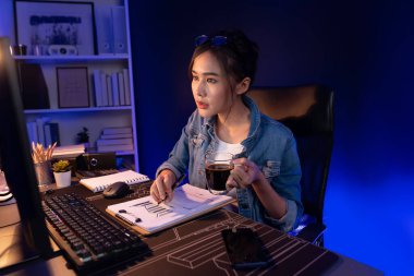 Elinde kahve fincanıyla bilgisayara bakan Asyalı güzel yaratıcı bir kadının iş piyasası grafik klasörü raporuna gece vakti işaret ettiğini düşünmek. Taktik.