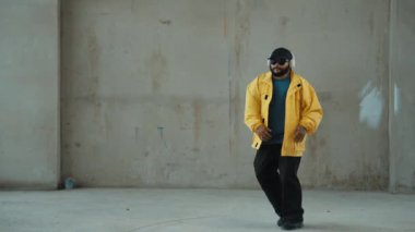 Hippi sokak, şehir merkezinde ayak izleri gösteriyor ya da pratik yapıyor. Break dansçının hareket halindeyken kulaklıktan müzik dinlediği sahne. Açık hava sporu 2024. Gri arka plan. Hip hop modası. hiphop.