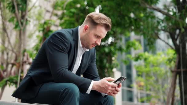 Professionell Affärsman Sitter Parken Medan Arbetar Telefon Genom Att Läsa — Stockvideo