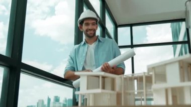 Gökdelen manzarasına bakarken yürüyen profesyonel mimar mühendisi. Masaya yerleştirilmiş ev modeliyle pencereye bakarken yetenekli proje yöneticisi proje planını tutuyor. Tasarım. İzleme