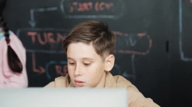 Çocuğun dizüstü bilgisayar mühendisliği kodunu ve yazım programını kullanırken STEM teknoloji sınıfında kontrol sahibi olan çeşitli çocuklardan oluşan bir grubun hemen karatahtayla yazılmış hali. Etkinlik.