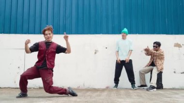 Genç Asyalı dansçı hip hop tarzında dans ediyor ve çok kültürlü arkadaşları duvarın arkasında tezahürat yapıyor. Çekici yakışıklı adam mavi arka planda kollarını uzatıyor. Açık hava sporu 2024 hiphop..